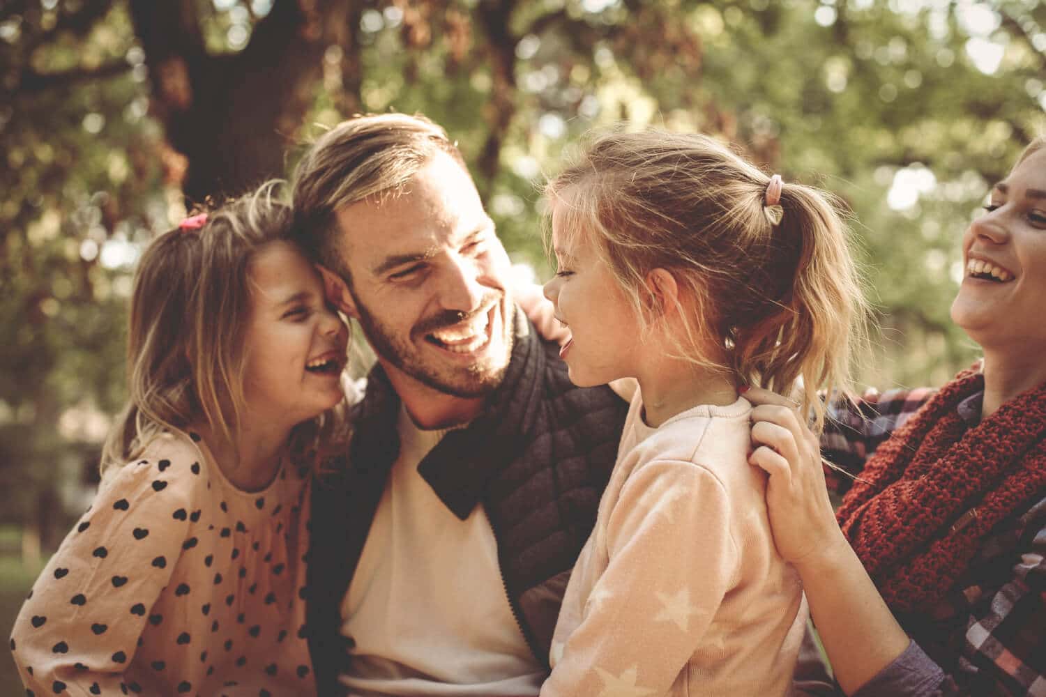A smiling family sitting outdoors, featuring two parents and two young daughters laughing together in boise id