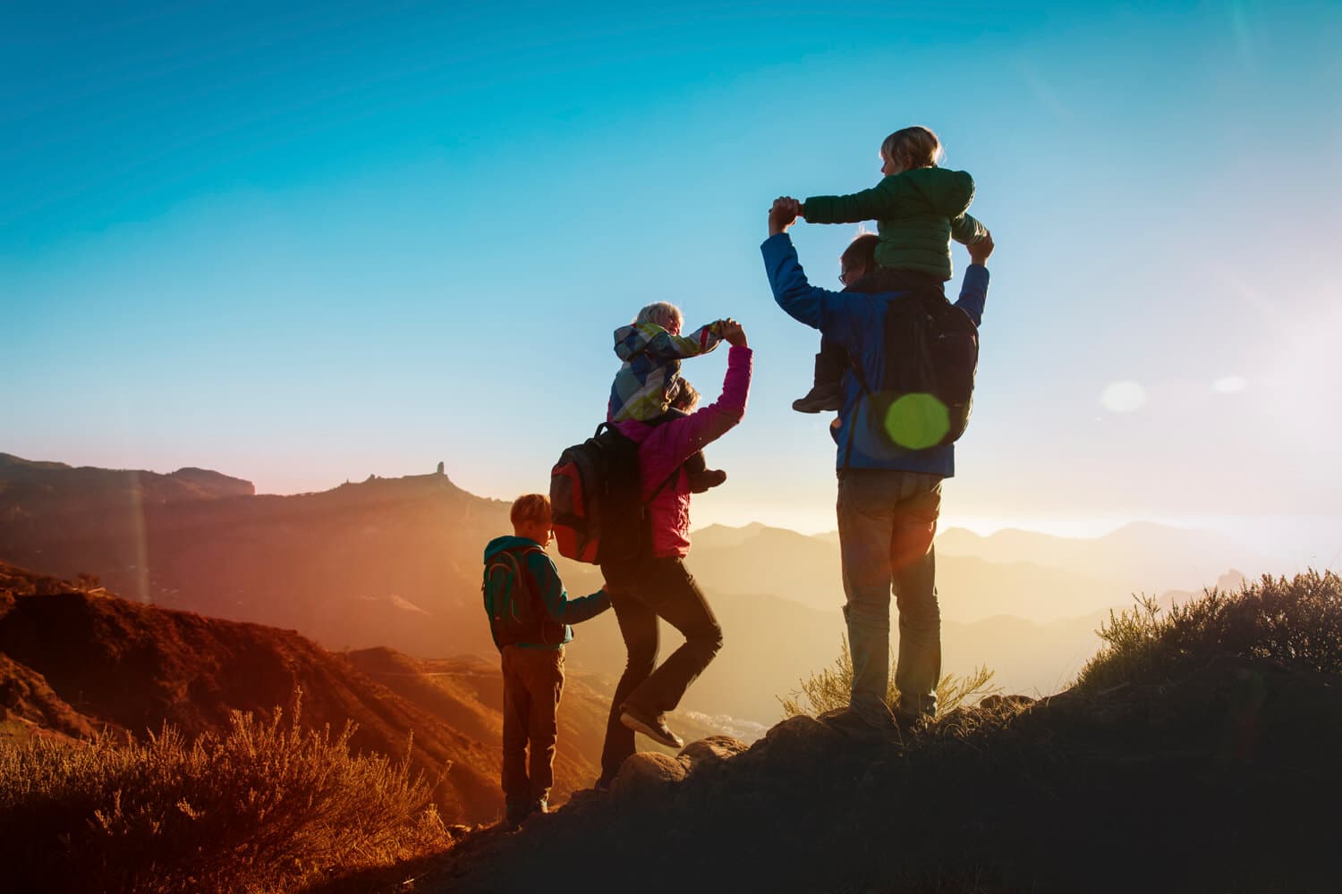 A family of four hiking on a mountain trail during sunset, with parents holding their children on shoulders in boise id